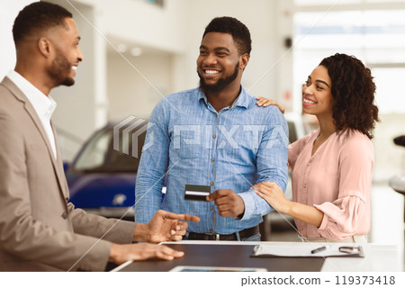 Afro Couple Buying Car Giving Seller Credit Card Standing In Auto Dealership Office. Selective Focus 119373418