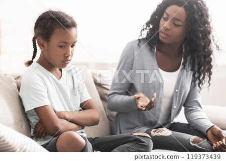 Disobedient kid. Strict black mom looking at her little daughter with rebuke, sitting on sofa at home, closeup 119373439