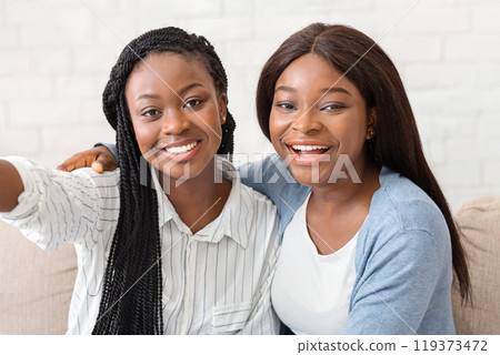 Selfie time. Two cheerful black girlfriends taking self-photograph, having fun together at home, closeup Selfie time. Two cheerful black girlfriends taking self-photograph, having fun together at home, closeup 119373472