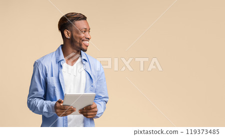 Happy African American Man Holding Tablet Computer Looking Aside Standing On Yellow Background In Studio. Panorama, Free Space 119373485