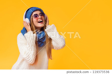 Emotional winter girl with wireless earphones and sunglasses enjoying music, pink background, free space 119373536