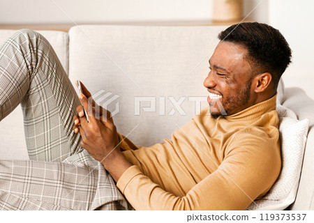 Mobile App. Relaxed Black Guy Using Smartphone Playing Games Lying On Sofa At Home. Mobile App. Relaxed Black Guy Using Smartphone Playing Games Lying On Sofa At Home. 119373537