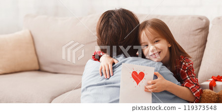 Happy Fathers Day concept. Sweet little girl hugging her dad, holding self made greeting card, home interior 119373548