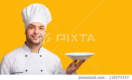 Smiling Chef Man Serving Dish Holding Empty Plate Standing Over Yellow Background. Studio Shot 119373557