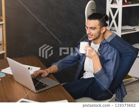 Short break for yoga in office. Flexible man practicing yoga at workplace, while typing on laptop and having coffee, copy space. Active employee at work, healthy lifestyle concept 119373602