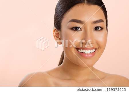 Close-up portrait of a young Asian woman with long black hair and a bright smile. Her skin appears smooth and clear, and she is wearing minimal makeup. The background is soft pink 119373623