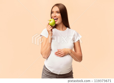 Pregnancy And Nutrition. Pregnant Woman Eating Apple Touching Belly Posing Over White Studio Background. Pregnancy And Nutrition. Pregnant Woman Eating Apple Touching Belly Posing Over White Studio Background. 119373671