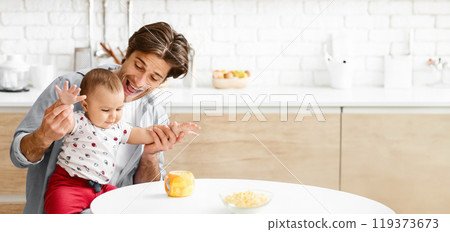 This image shows a father and his young son playing in a kitchen. The father is holding his son, who is reaching out with his hand and smiling. The father is also smiling, copy space 119373673