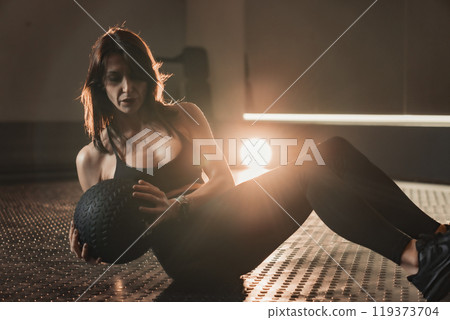 A dedicated young woman performs medicine ball exercises in a modern gym, demonstrating her commitment to achieving personal fitness goals and aspirations during an intense workout 119373704