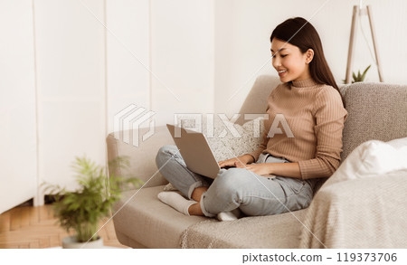 Teen Girl Surfing Internet on Laptop Computer, Sitting on Sofa with Crossed Legs, Free Space Teen Girl Surfing Internet on Laptop Computer, Sitting on Sofa with Crossed Legs, Free Space 119373706