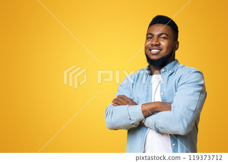 Confident black millenmial man standing with his arms crossed, smiling and looking at camera, yellow studio background with copy space Confident black millenmial man standing with his arms crossed, smiling and looking at camera, yellow studio background with copy space 119373712