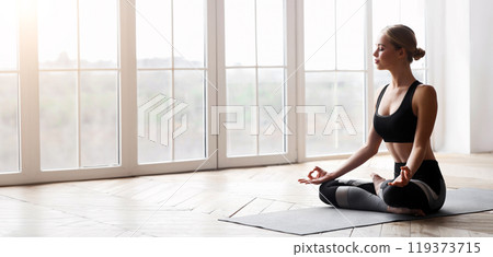 Yoga girl with closed eyes meditating in lotus pose in studio, no stress concept, free space 119373715