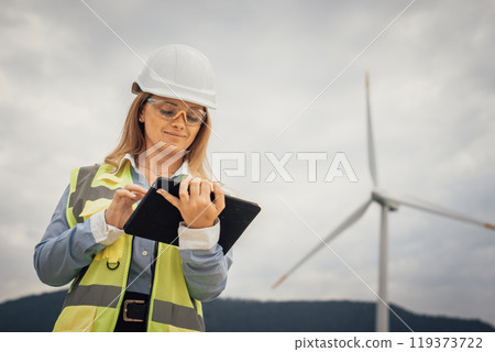 A skilled female engineer inspects a wind turbine with her tablet, ensuring efficiency and optimal performance, contributing significantly to sustainability and renewable energy initiatives 119373722