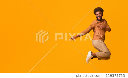 Cheerful young black man having fun over orange background, jumping in the air and showing tricks 119373733