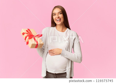 Baby Shower Concept. Happy Pregnant Lady Holding Wrapped Gift Box Looking At Camera Standing Over White Background. Studio Shot 119373745
