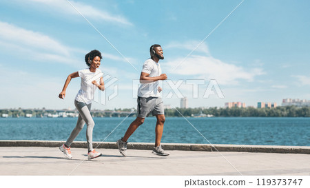 Early morning jogging. Positive black spouses running outdoor along river embankment. Panorama, empty space for text Early morning jogging. Positive black spouses running outdoor along river embankment. Panorama, empty space for text 119373747