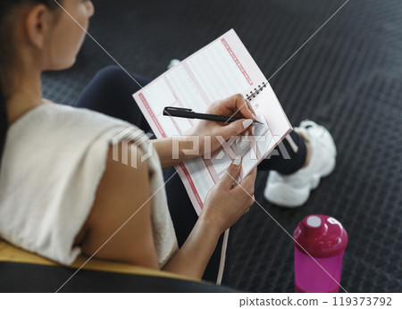 Workout planning. Young woman making her workout schedule in notebook indoors, above view 119373792
