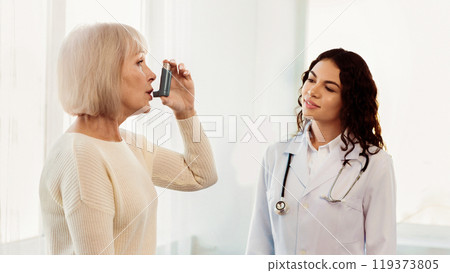 Medical Advice. Elderly woman using asthma inhaler, mexican doctor watching, free space, panorama Medical Advice. Elderly woman using asthma inhaler, mexican doctor watching, free space, panorama 119373805