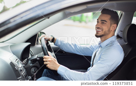 Excited arab guy going to office in the morning, driving his car, side view, copy space. Cheerful middle-eastern young man looking at the road, sitting inside luxury automobile, going home from job 119373851