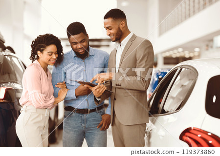 Car Rent. Afro Salesman Offering Couple Automobile Standing In Auto Rental Office. Car Rent. Afro Salesman Offering Couple Automobile Standing In Auto Rental Office. 119373860