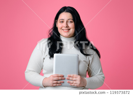 Smiling Plus Size Girl Posing With Digital Tablet In Hands, Standing Over Pink Background With Free space Smiling Plus Size Girl Posing With Digital Tablet In Hands, Standing Over Pink Background With Free space 119373872