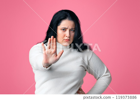 No Bullying Concept. Serious overweight girl showing stop gesture, standing with outstretched hand over pink background, copy space 119373886