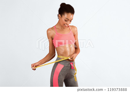 Slim African American Girl Measuring Waist Using Tape Over Pink Studio Background. Weight Loss Concept. Free Space Slim African American Girl Measuring Waist Using Tape Over Pink Studio Background. Weight Loss Concept. Free Space 119373888