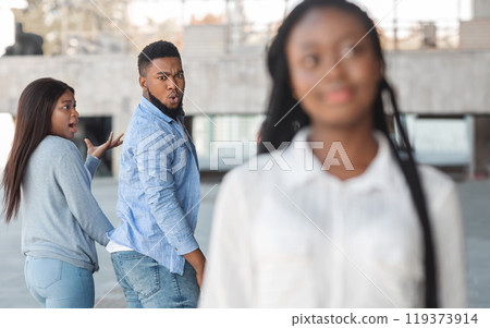 Distracted african american guy turning around and looking to another woman while walking with his girlfriend Distracted african american guy turning around and looking to another woman while walking with his girlfriend 119373914