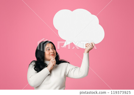 Pensive plus size woman holding and looking at blank speech bubble over her head, standing on pink background Pensive plus size woman holding and looking at blank speech bubble over her head, standing on pink background 119373925