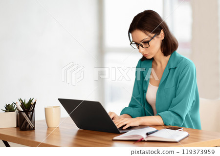 Home Office. Portrait of young female manager wearing specs and brown shirt using laptop, working remotely. Copy space Home Office. Portrait of young female manager wearing specs and brown shirt using laptop, working remotely. Copy space 119373959
