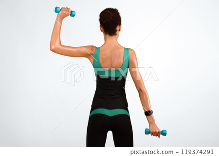 Unrecognizable Black Girl Working Out With Dumbbells Standing Back To Camera Over Yellow Studio Background. Biceps Exercises 119374291