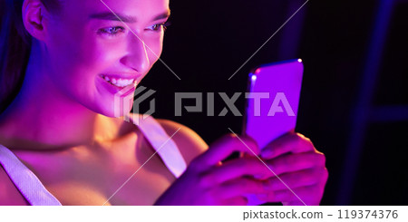 Girl surfing internet on phone in pink neon light in dark room, panorama Girl surfing internet on phone in pink neon light in dark room, panorama 119374376