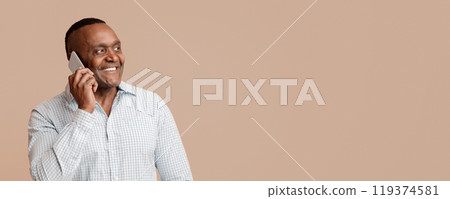 Pleasant talk. Cheerful afro man talking on mobile phone, orange panorama background with empty space Pleasant talk. Cheerful afro man talking on mobile phone, orange panorama background with empty space 119374581
