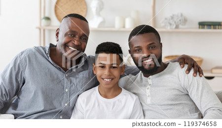 Handsome Senior African Man Embracing His Son And Grandson At Home And Posing To Camera Together, Panorama 119374658