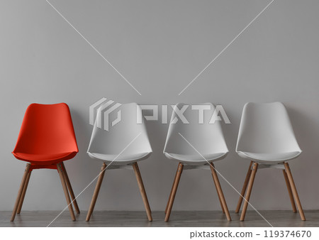 Three vacant white chairs and one red on gray wall background in office or room. Simple minimalist interior, nobody, free space. Job recruiting, leadership and business due covid-19 virus, mockup 119374670