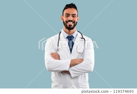 Portrait Of Cheerful Arab Doctor Man Smiling To Camera Posing With Stethoscope Crossing Hands Over Blue Background. Confident Cardiologist Standing In Studio. Successful Medical Career Portrait Of Cheerful Arab Doctor Man Smiling To Camera Posing With Stethoscope Crossing Hands Over Blue Background. Confident Cardiologist Standing In Studio. Successful Medical Career 119374693