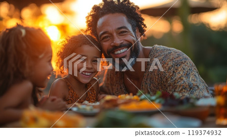 A father enjoys quality time with his two daughters at a sunset picnic, surrounded by delicious food and laughter, creating cherished memories together. 119374932