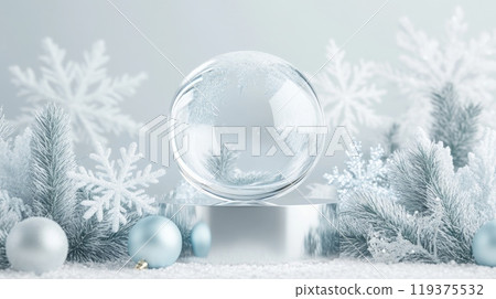 A clear glass sphere sits atop a reflective surface, surrounded by delicate snowflakes and frosty green foliage. The soft, wintry ambiance creates a serene atmosphere, perfect for seasonal decor. 119375532