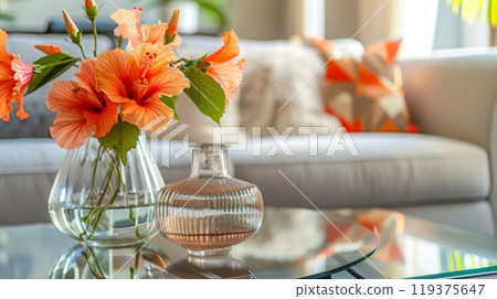 Vibrant hibiscus flowers in a glass vase rest on a coffee table, complementing a stylish living room with cushions. Vibrant hibiscus flowers in a glass vase rest on a coffee table, complementing a stylish living room with cushions. 119375647