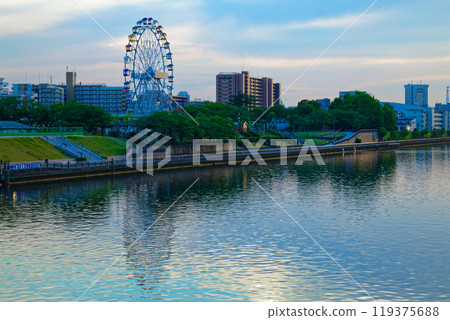 The Ferris wheel at Arakawa Amusement Park and the scenery reflected on the Sumida River. Evening view. Sunset. The Ferris wheel at Arakawa Amusement Park and the scenery reflected on the Sumida River. Evening view. Sunset. 119375688