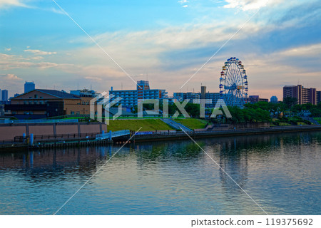 The Ferris wheel at Arakawa Amusement Park and the scenery reflected on the Sumida River. Evening view. Sunset. The Ferris wheel at Arakawa Amusement Park and the scenery reflected on the Sumida River. Evening view. Sunset. 119375692