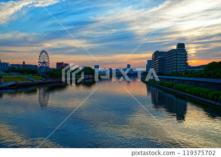 The Ferris wheel at Arakawa Amusement Park and the scenery reflected on the Sumida River. Evening view. Sunset. The Ferris wheel at Arakawa Amusement Park and the scenery reflected on the Sumida River. Evening view. Sunset. 119375702