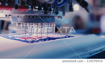 An embroidery machine meticulously stitches a colorful logo onto a piece of fabric in a crafting workshop. 119376419