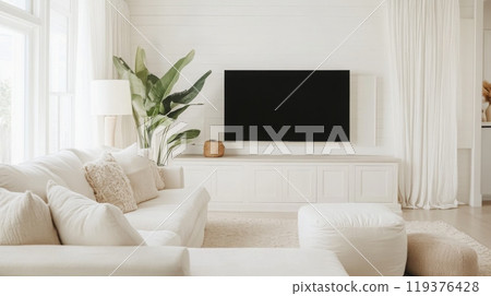 A bright and airy living room with a large, white sectional sofa, a flat-screen TV mounted above a white cabinet, and a small, white ottoman 119376428