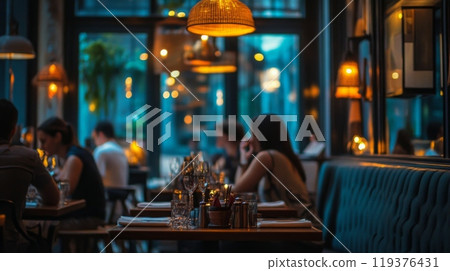 A cozy restaurant filled with warm, ambient lighting creates an inviting atmosphere for diners enjoying their meals. Guests engage in conversation as they savor their dishes in a relaxed setting. 119376431