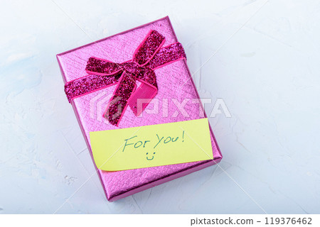 A shiny pink gift box adorned with a ribbon and a yellow note For You on a soft background. 119376462