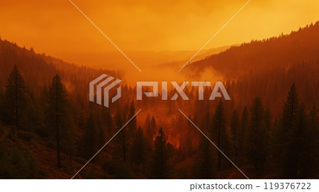 Thick smoke from a wildfire creates an eerie orange haze that blankets a mountainous forest, obscuring the trees and altering the natural landscape at sunset. 119376722