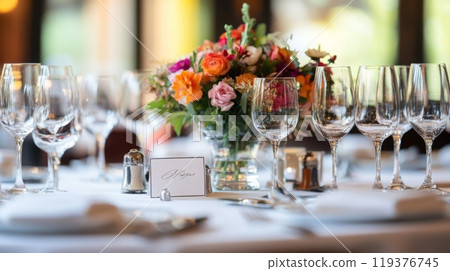 A beautifully arranged dining table features a vibrant floral centerpiece surrounded by sparkling glassware, set for an exquisite evening meal. 119376745