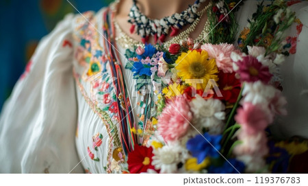 A person showcases a beautifully embroidered traditional outfit, decorated with vibrant flowers during a cultural event. 119376783