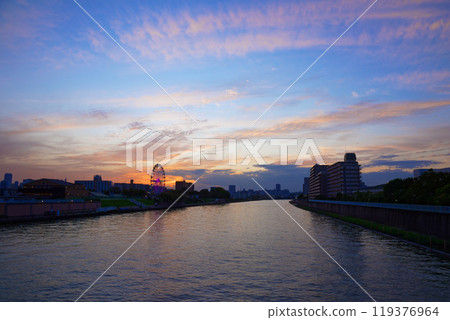 The Ferris wheel at Arakawa Amusement Park and the scenery reflected on the Sumida River. Evening view. Sunset. The Ferris wheel at Arakawa Amusement Park and the scenery reflected on the Sumida River. Evening view. Sunset. 119376964